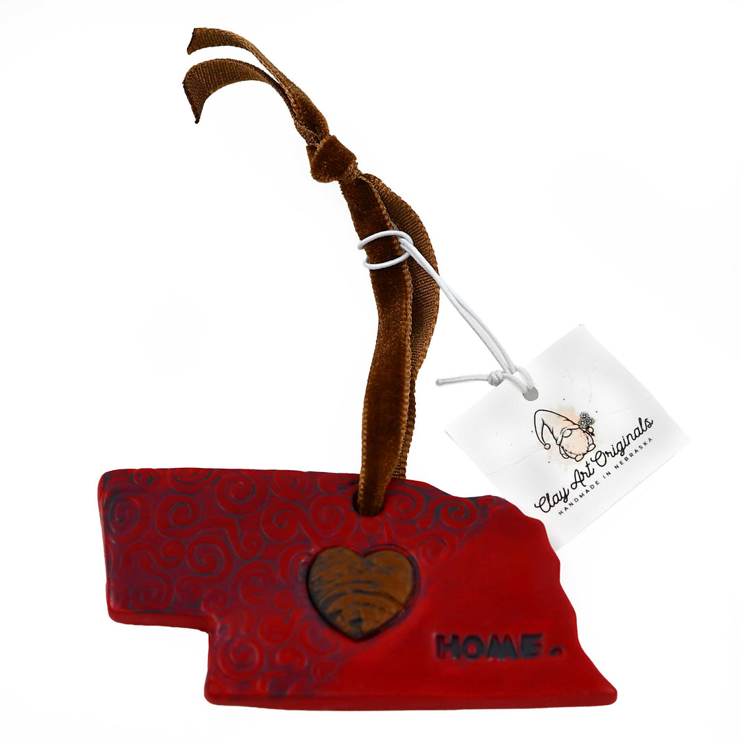 Nebraska-shaped ornament with a heart and 'Home' text, attached to a brown ribbon with a tag.