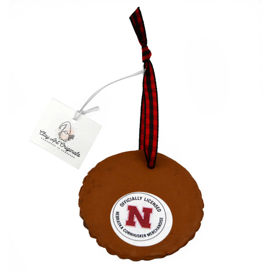 Back of brown ornament with a red and black plaid ribbon and Nebraska logo on a white background