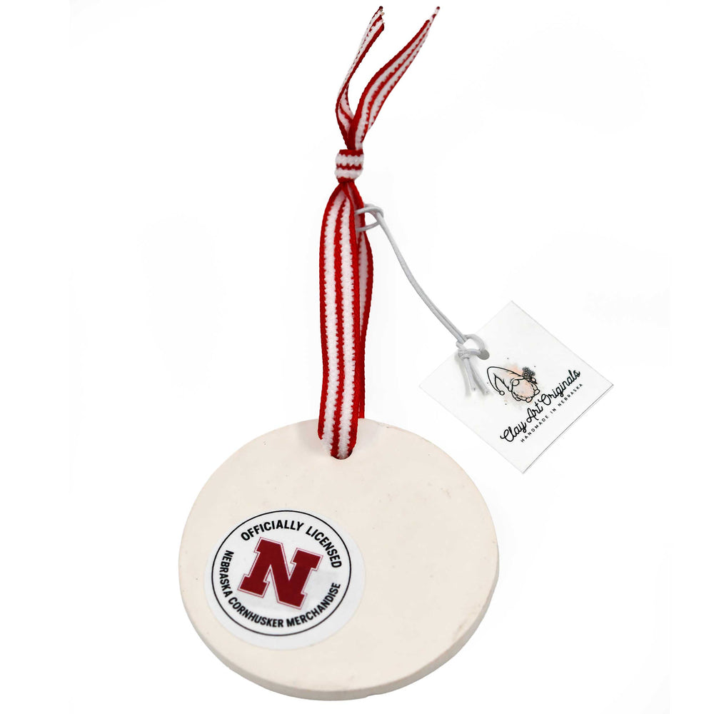 Nebraska-themed ceramic ornament with red and white ribbon on a white background