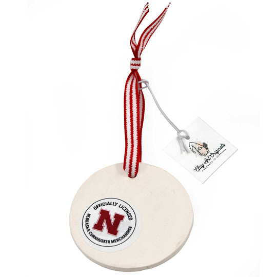 Nebraska-themed ceramic ornament with red and white ribbon on a white background