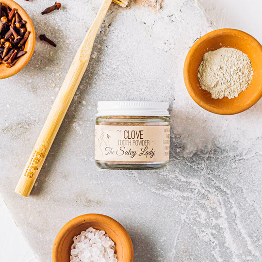 Jar of clove tooth powder with wooden spoon and ingredients on a textured surface