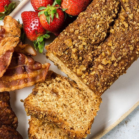 Loaf of bread with slices cut, bacon, and strawberries on a plate.