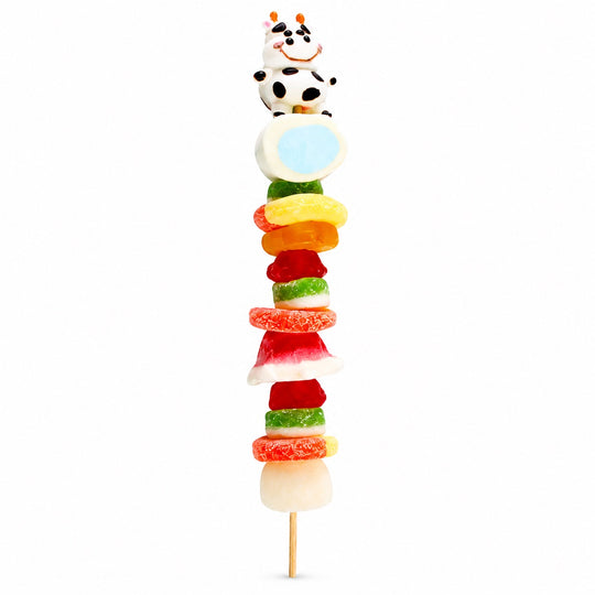 Cow candy kabob featuring a black-and-white cow candy topper and assorted fruit-flavored candies on a wooden skewer, isolated on a white background.