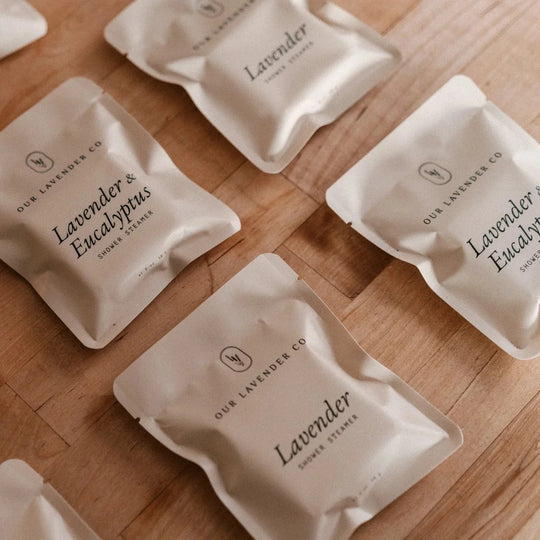 Beige shower packets labeled 'Lavender & Eucalyptus' on a wooden surface
