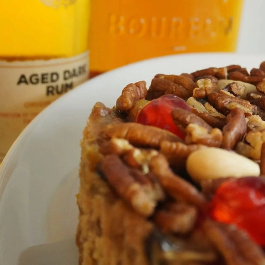 Slice of fruitcake with nuts and cherries on a plate with bottles of rum in the background.
