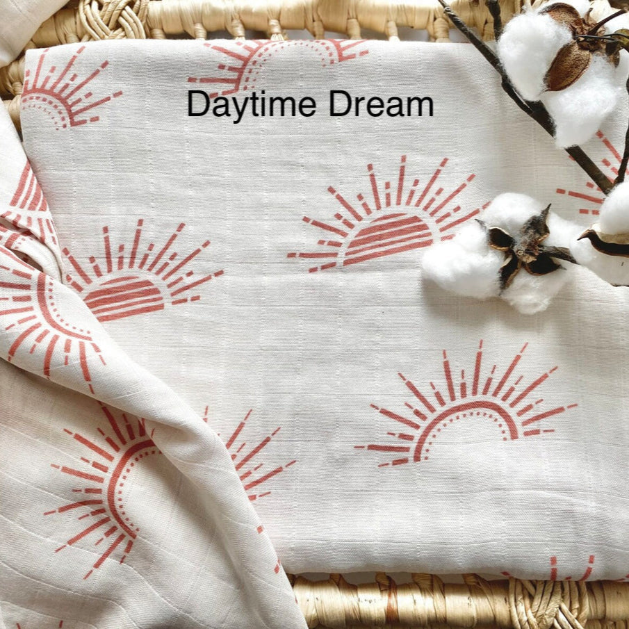 Fabric with sun patterns and 'Daytime Dream' text, surrounded by cotton and a woven basket.