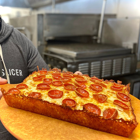 Rectangular pizza with pepperoni on a wooden board in a kitchen setting