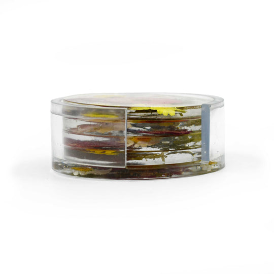 A clear cylindrical resin keepsake jar with a matching lid, containing layered dried botanical elements in yellow, green, and brown, set against a plain white background.