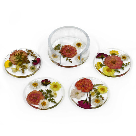 Five clear resin coasters with embedded pressed flowers, arranged on a white background. Four coasters are flat circles and one is a short cylindrical tumbler, all containing floral designs with pink, yellow, white, and green elements.