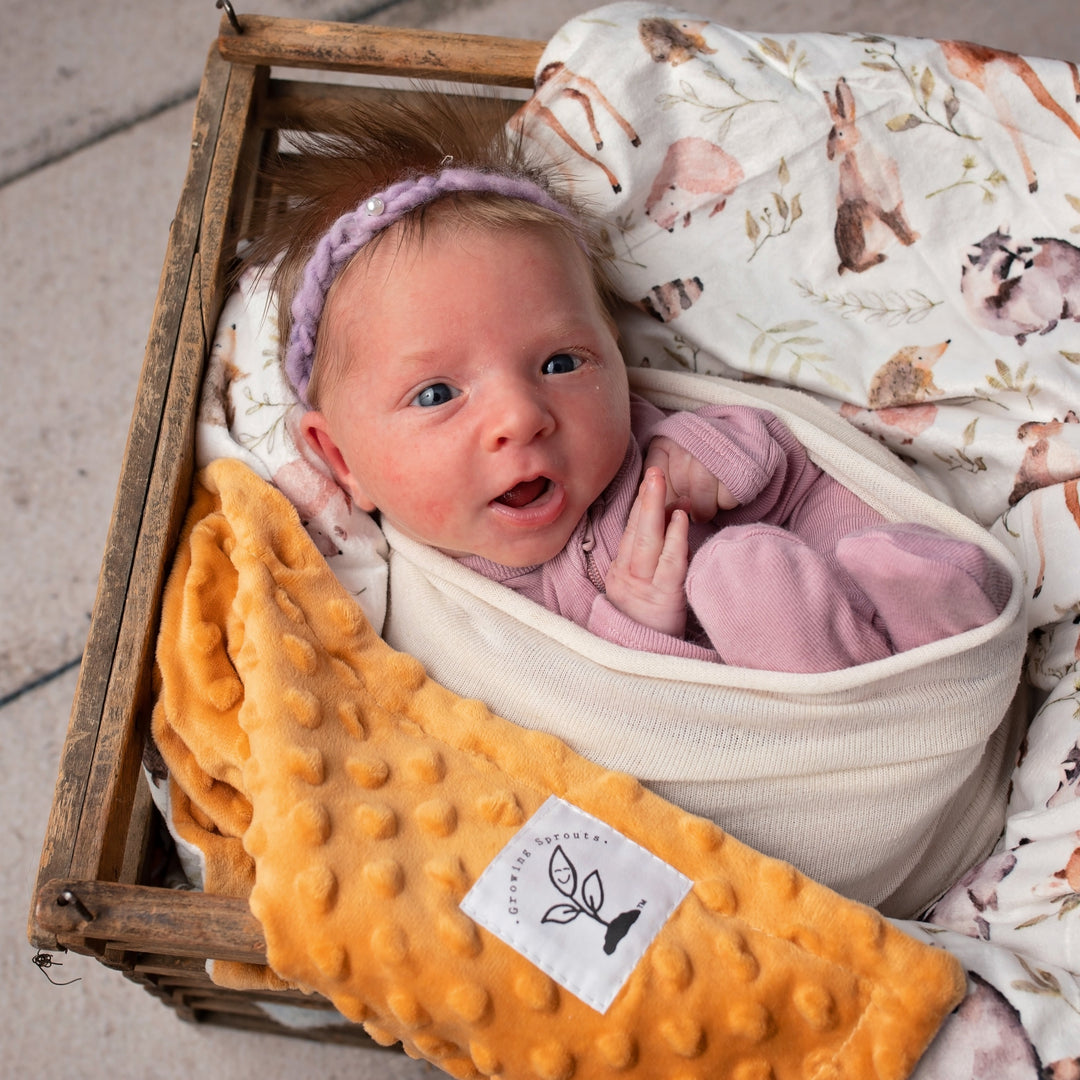 Newborn baby wrapped in a pink blanket with a textured yellow blanket and a patterned blanket in the background.