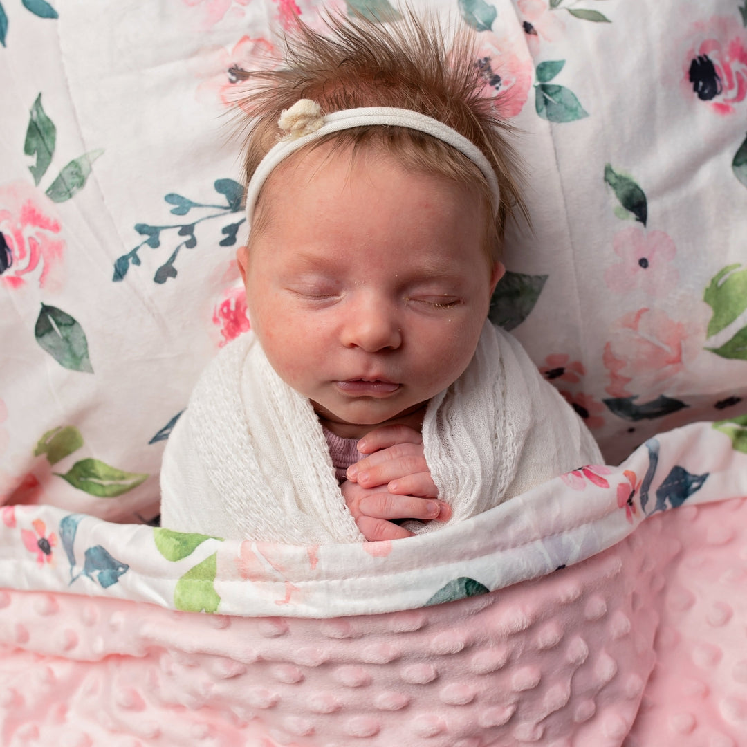 Newborn baby wrapped in a pink blanket with a floral-patterned background