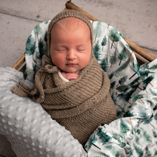 Newborn baby wrapped in brown fabric with a green and white patterned blanket