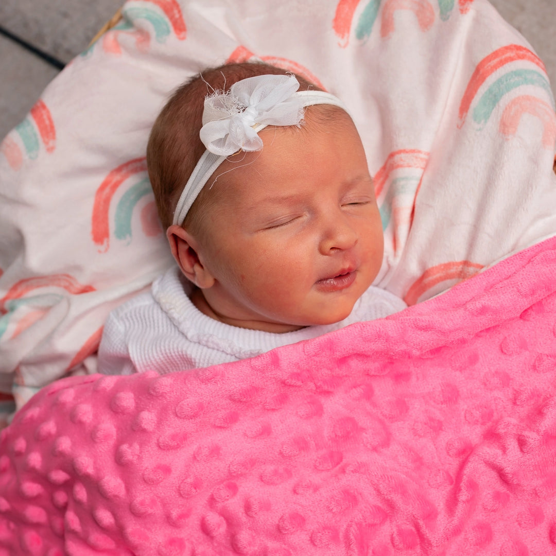 Newborn baby sleeping in a basket with pink blanket and white headband.
