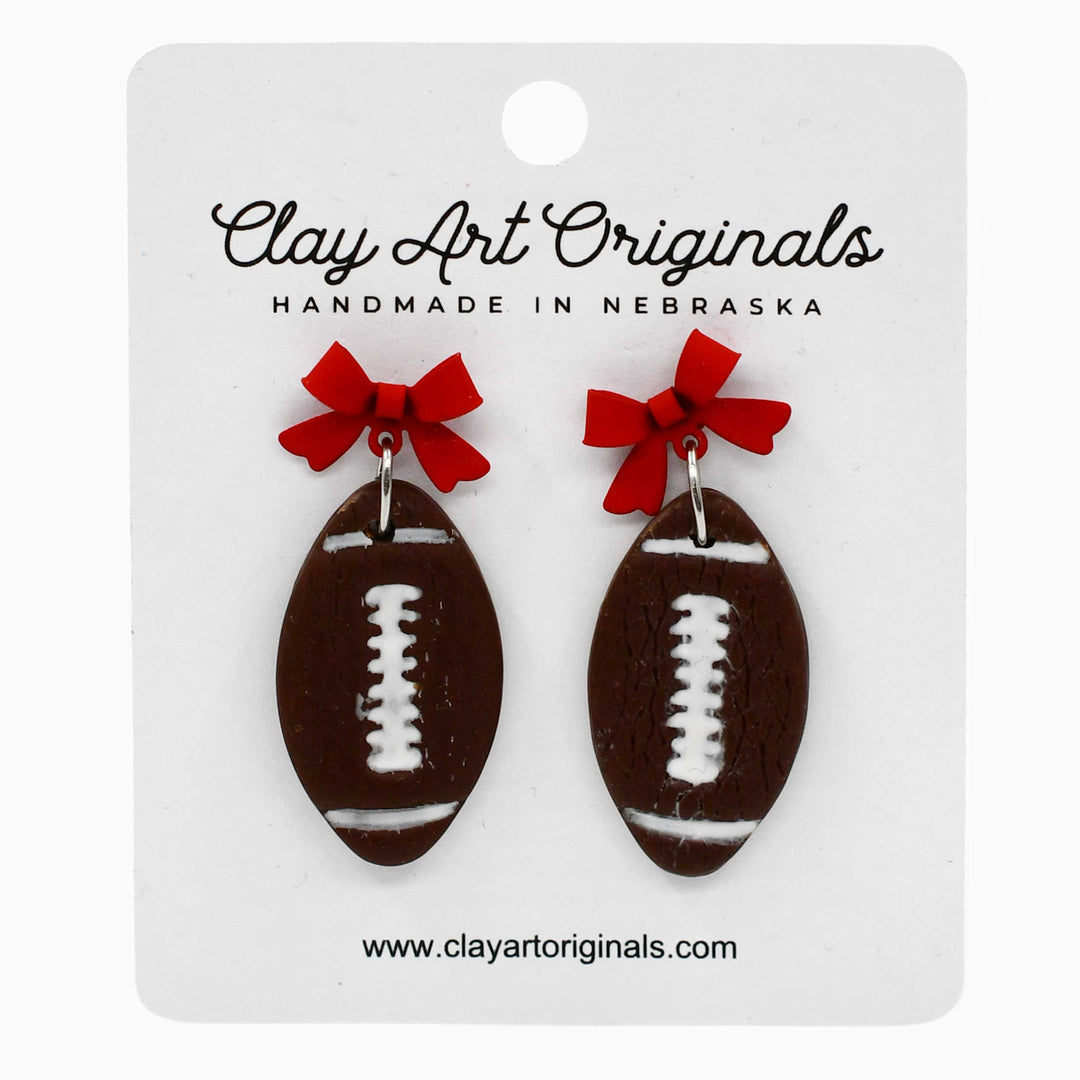 Football-shaped earrings with red bows on a Clay Art Originals card.