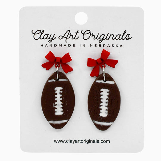 Football-shaped earrings with red bows on a Clay Art Originals card.
