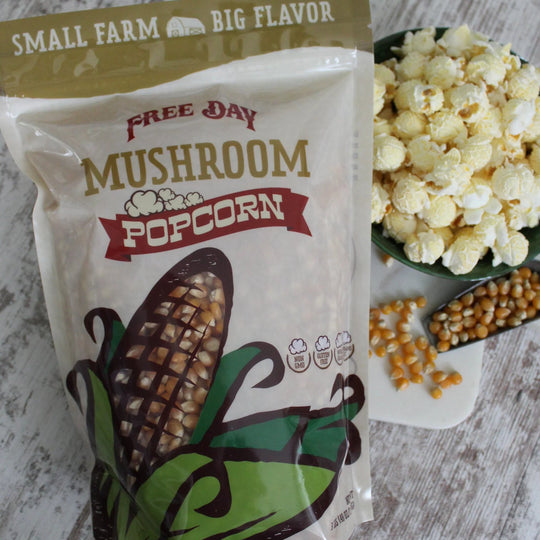 Bag of Free Day Mushroom Popcorn on a wooden surface with popcorn and corn kernels.