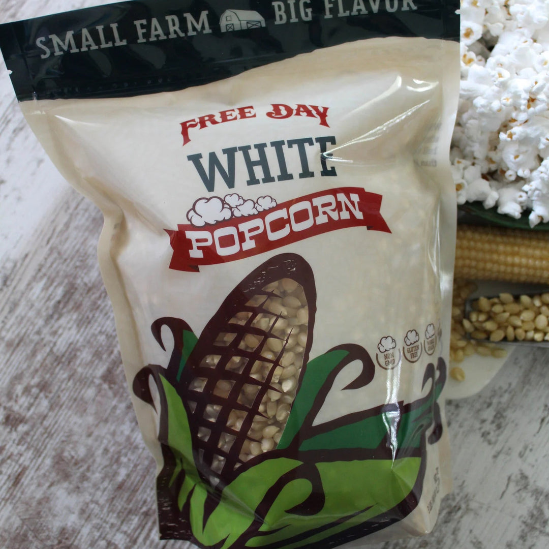 Bag of Free Day White Popcorn on a wooden surface with popcorn and corn in the background.