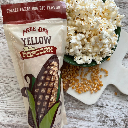 Free Day Yellow Popcorn bag with popcorn and kernels on a wooden surface