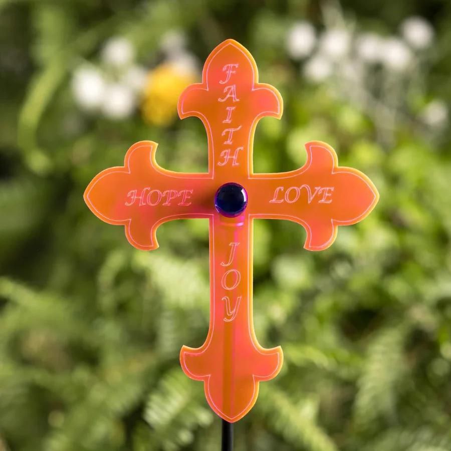 An orange glowing "Faith, Hope, Love, Joy" cross on a leafy background