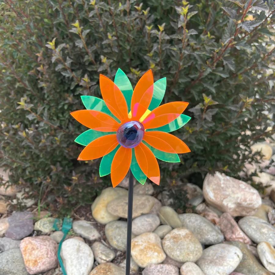 A glowing orange and green pinwheel against a bush