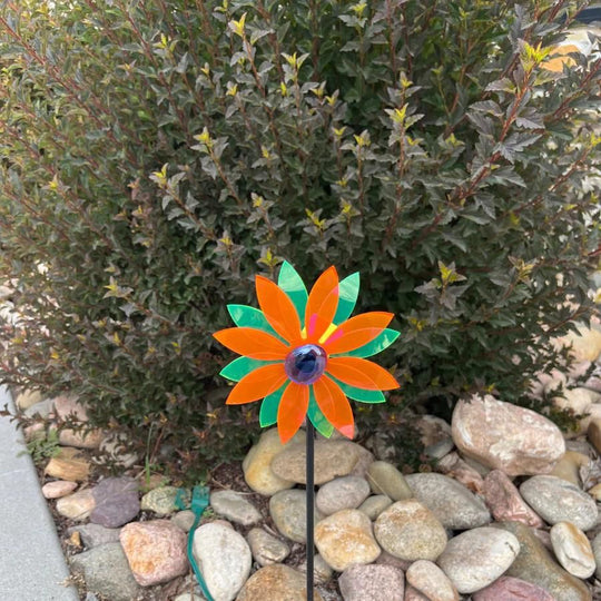 A glowing orange and green pinwheel against a bush