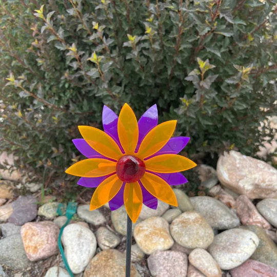 An orange and purple glowing pinwheel against a bush