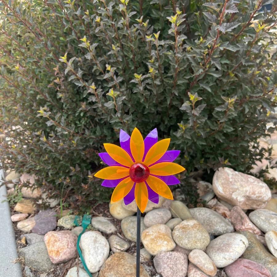 An orange and purple glowing pinwheel against a bush