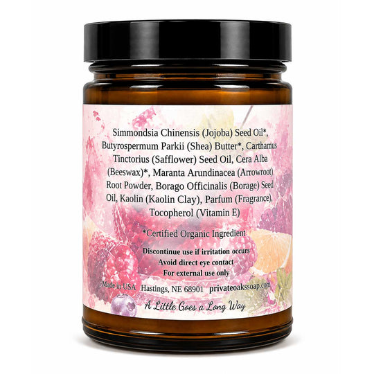 An amber glass jar with a black lid and a pink botanical label, photographed on a plain white background. The label lists ingredients such as Simmondsia Chinensis Seed Oil, Butter, Beeswax, and Root Powder, with the brand name 'A Little Goes a Long Way' at the bottom.