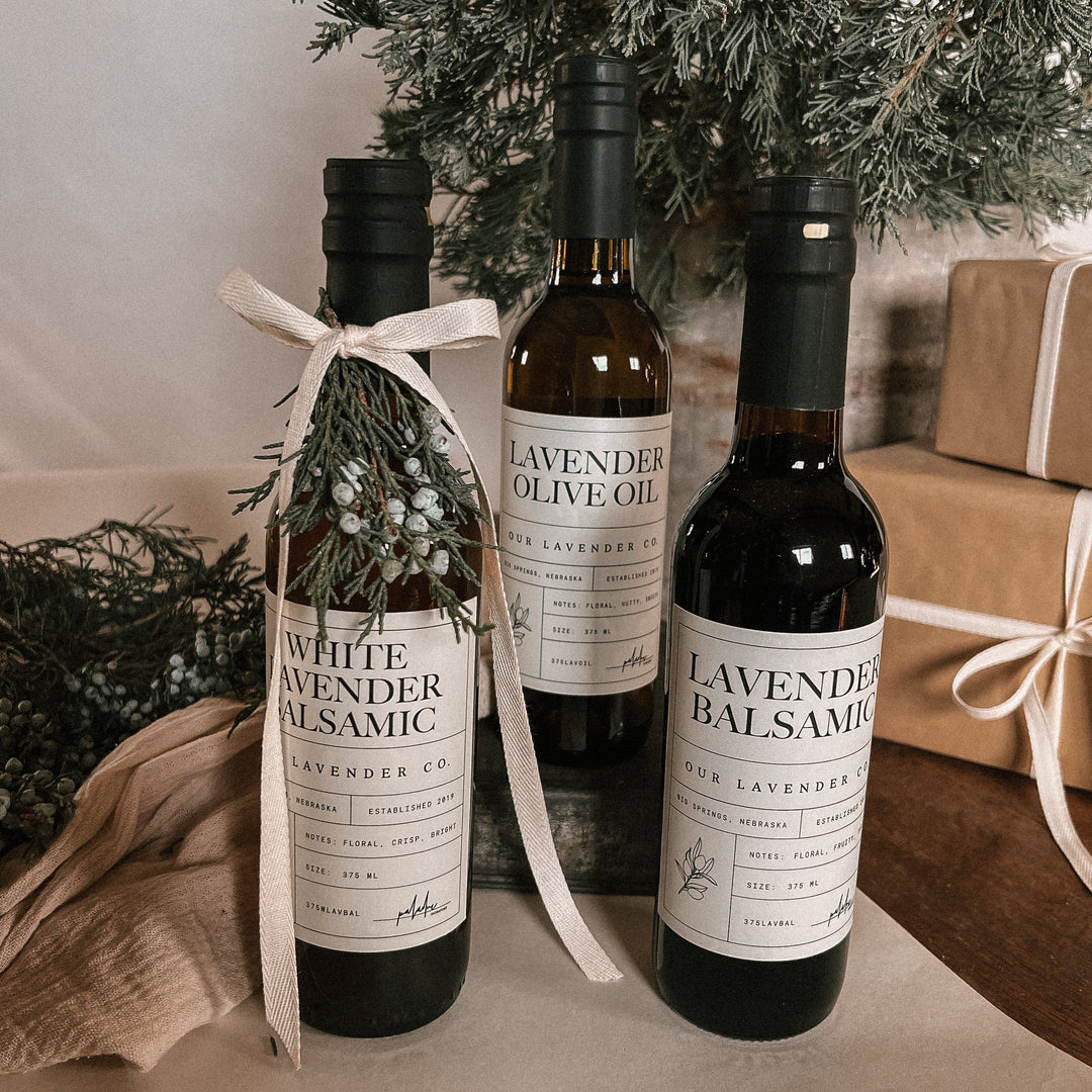 Three bottles of lavender products on a table with a Christmas tree and gift boxes in the background.