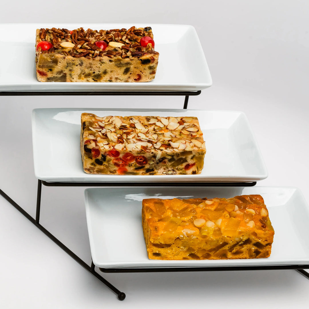 Three rectangular dishes of fruitcake on a tiered stand against a white background