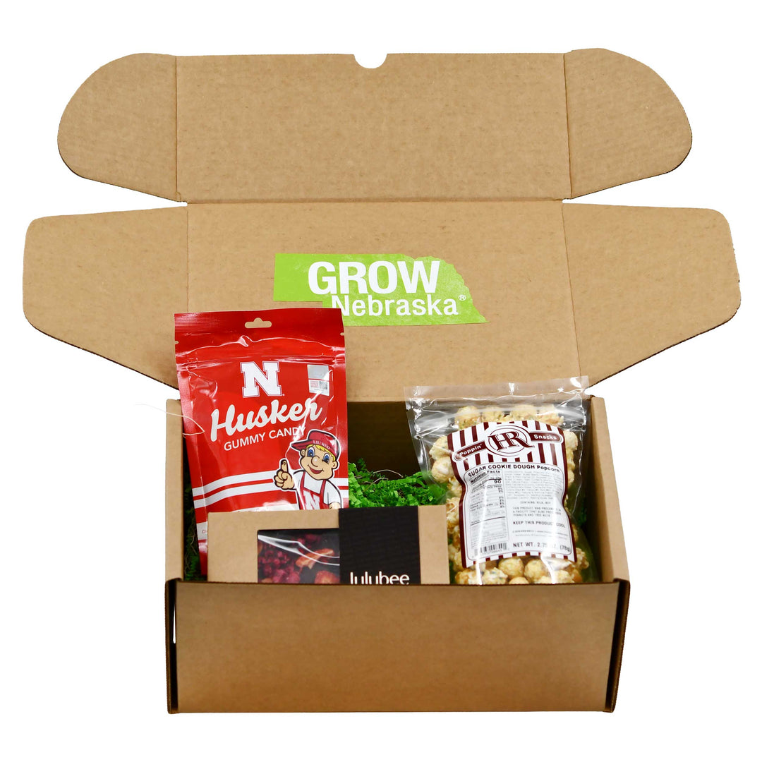 Open cardboard box with 'Grow Nebraska' branding, containing snacks and a magazine.
