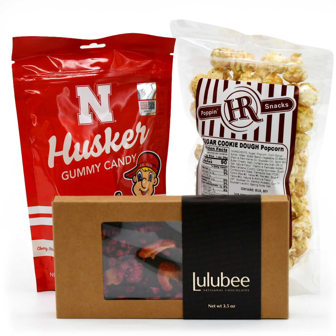 Snack package with Husker gummy candy, Lulubee box, and Poppin' Hot popcorn on a white background