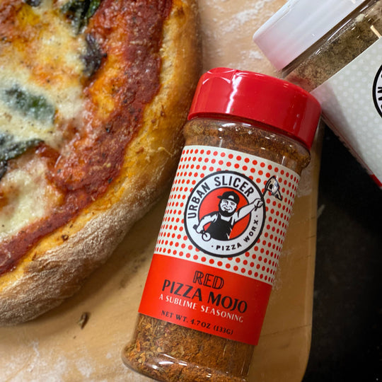 Jar of 'Red Pizza Mojo' seasoning next to a pizza on a cardboard box