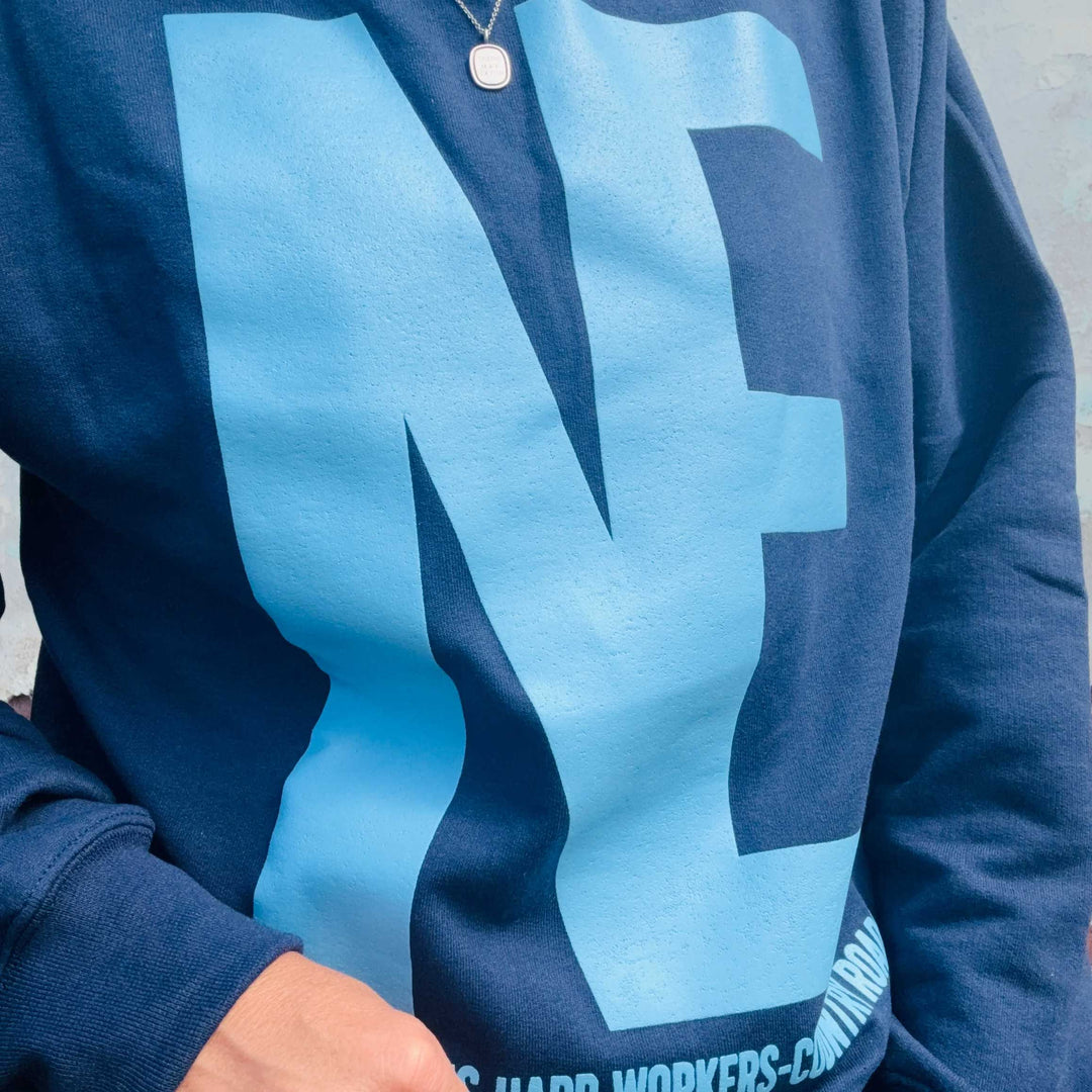 A close-up of a navy blue sweatshirt featuring a large light blue graphic letter 'N' on the front, worn by a person.