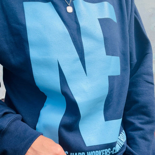 A close-up of a navy blue sweatshirt featuring a large light blue graphic letter 'N' on the front, worn by a person.