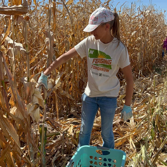 Person harvesting corn in a field wearing a branded t-shirt.