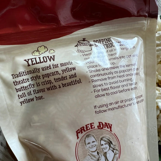 Yellow popcorn seasoning packet with text and a couple illustration, next to popcorn kernels.