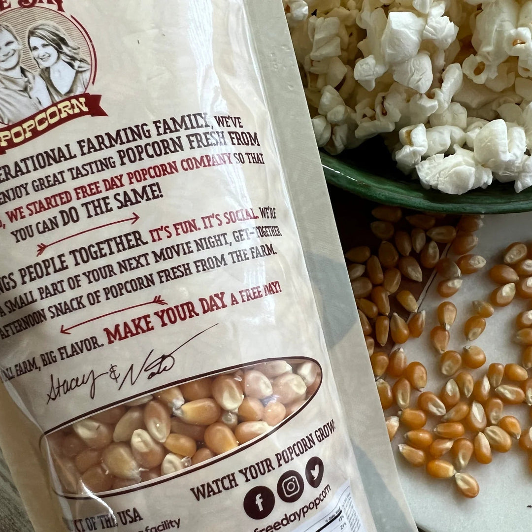 Popcorn bag with popcorn kernels and a bowl of popcorn on a white surface