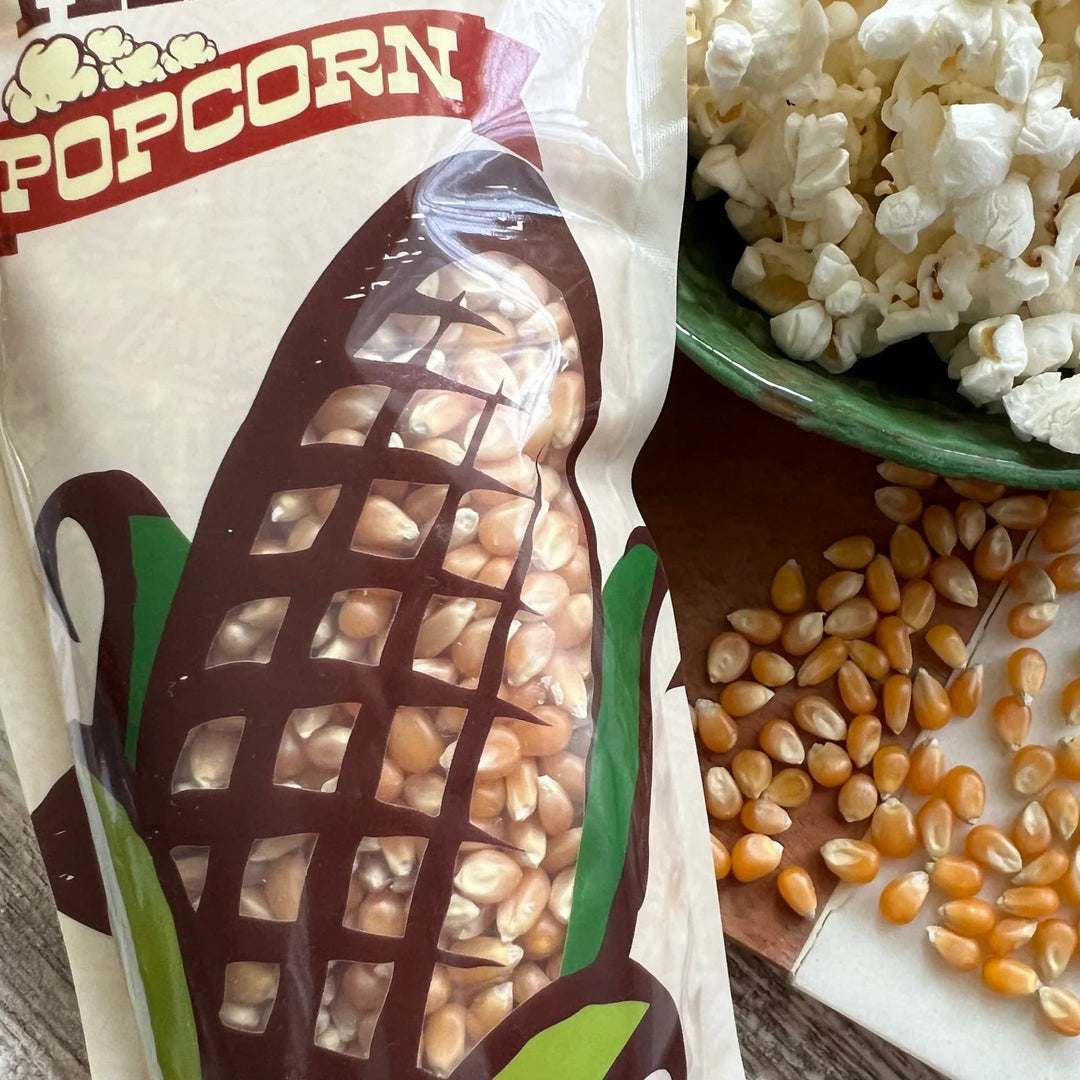 Popcorn bag with popcorn kernels and a bowl of popcorn on a wooden surface