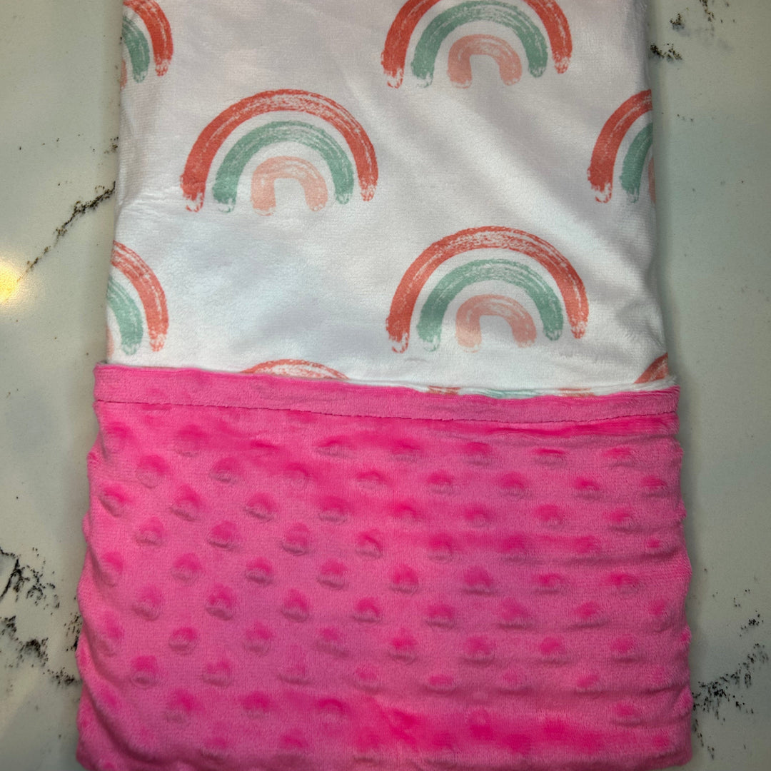 Folded fabric with rainbow pattern on top and pink textured bottom on a white surface.