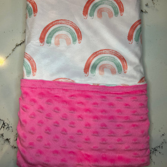 Folded fabric with rainbow pattern on top and pink textured bottom on a white surface.