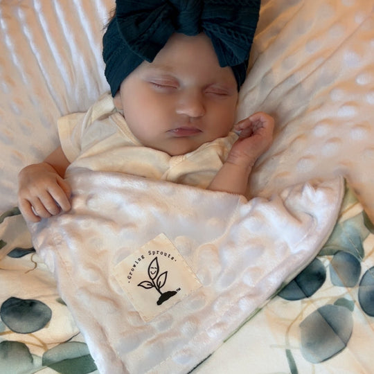 Newborn baby wrapped in a blanket with a visible brand logo, wearing a dark blue headband, on a textured surface.