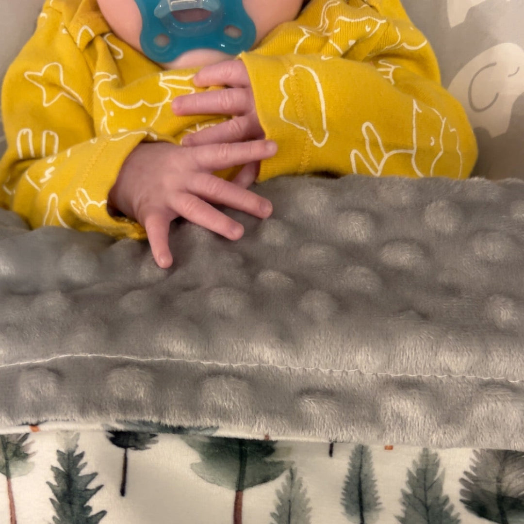 Child in yellow shirt with tree pattern holding a gray blanket with tree pattern