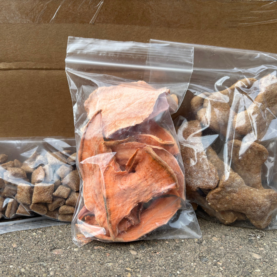 Three clear plastic bags containing dog treats on a cardboard box.