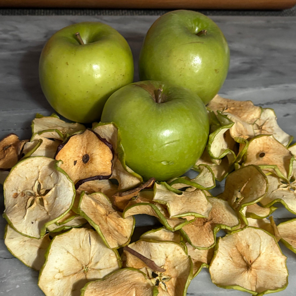 Three green apples surrounded by dried apple slices on a gray surface.