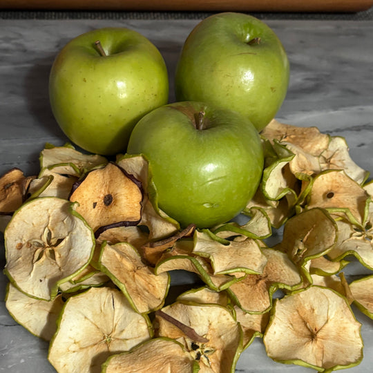 Three green apples surrounded by dried apple slices on a gray surface.