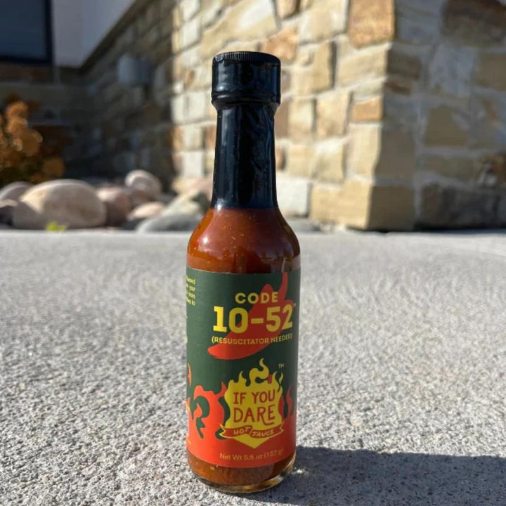 A bottle of Code 10-52 If You Dare Hot Sauce on a sidewalk