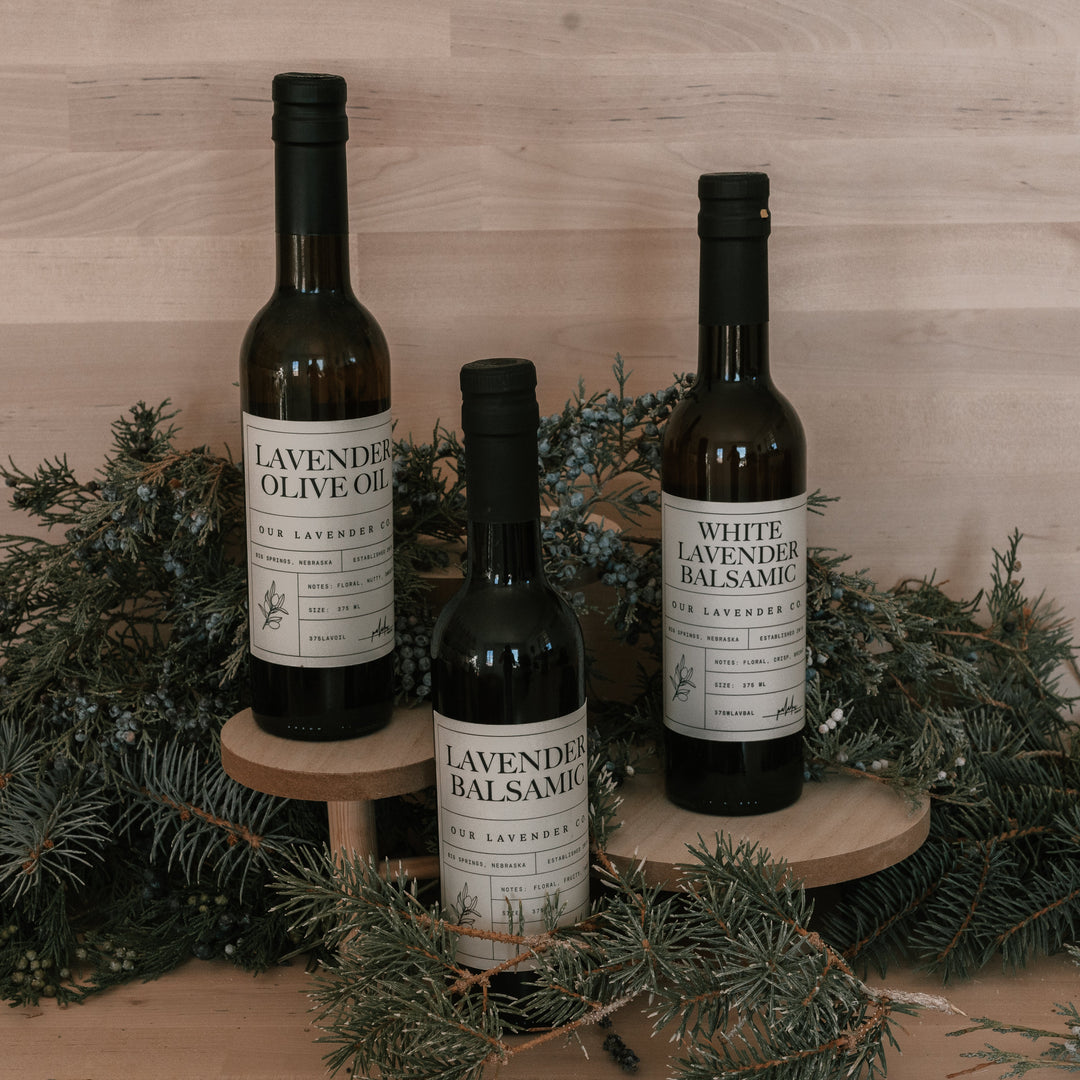 Three bottles of lavender-infused olive oil and balsamic on a wooden stand with a wooden background.