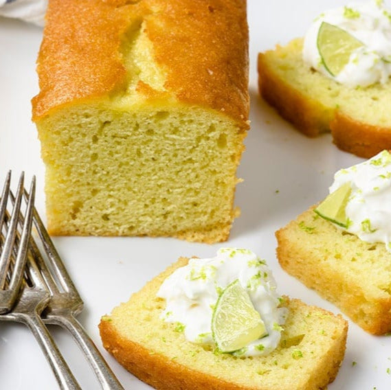 Sliced lime cake with whipped cream and lime slices on a white plate with silver forks.
