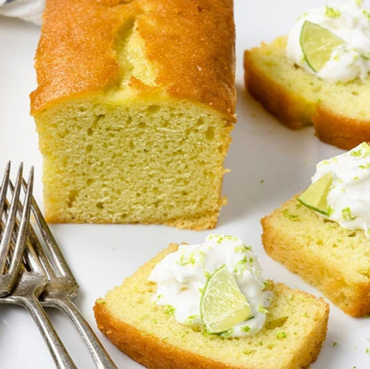 Sliced lime cake with whipped cream and lime slices on a white plate with silver forks.